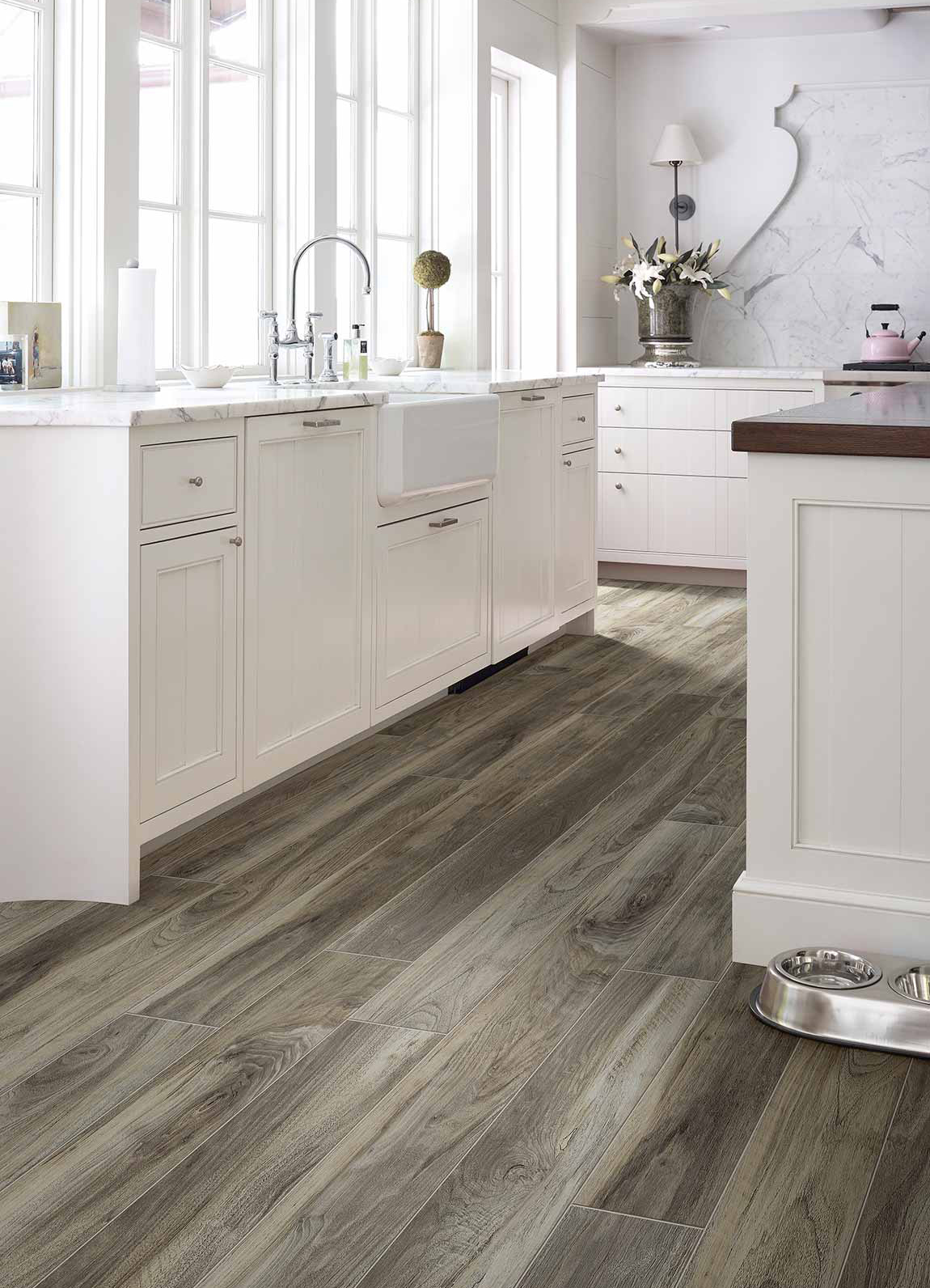 Wood-look laminate floor in kitchen by Shaw Floors. White cabinetry, kitchen island, and stone backsplash is featured.